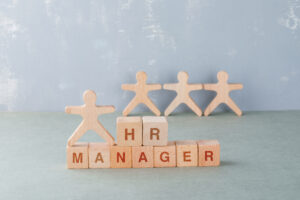 Hr Manager Concept With Wooden Blocks With Words On It, Wooden Human Figures On Sage Color Background High Angle View. Space For Text. Horizontal Image